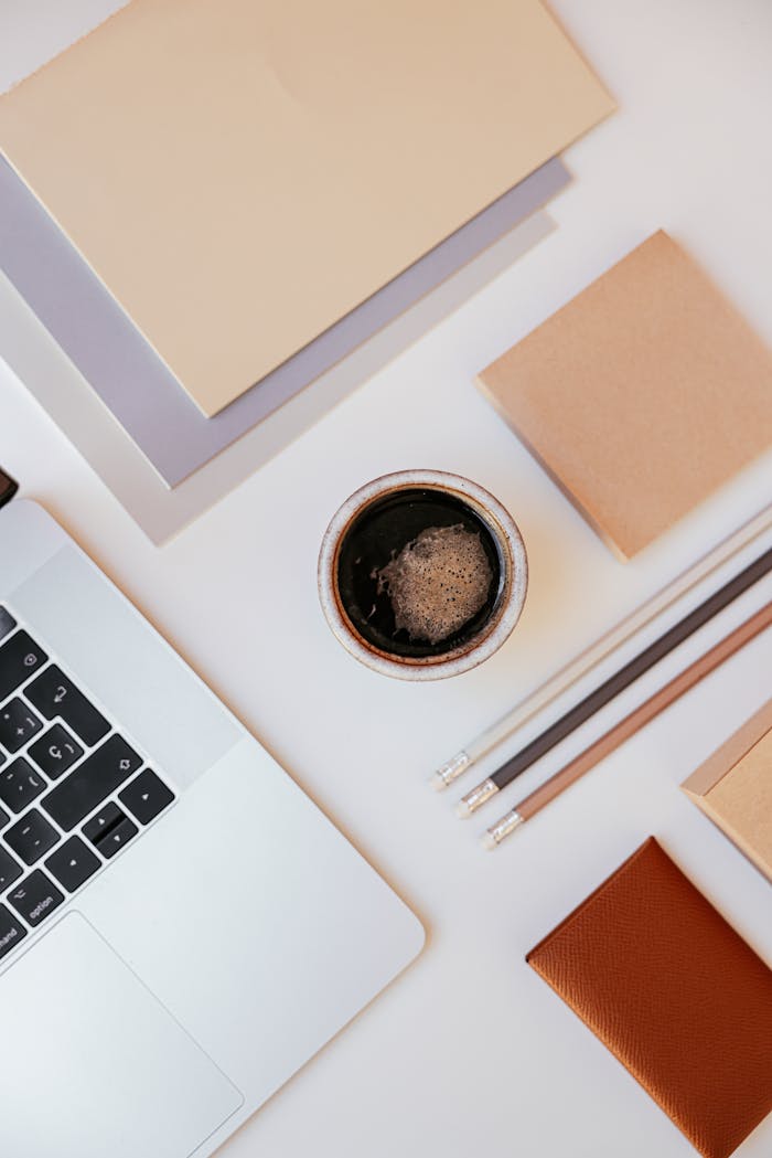 A top-down view of a minimalist desk setup featuring a laptop, coffee, and stationery items.